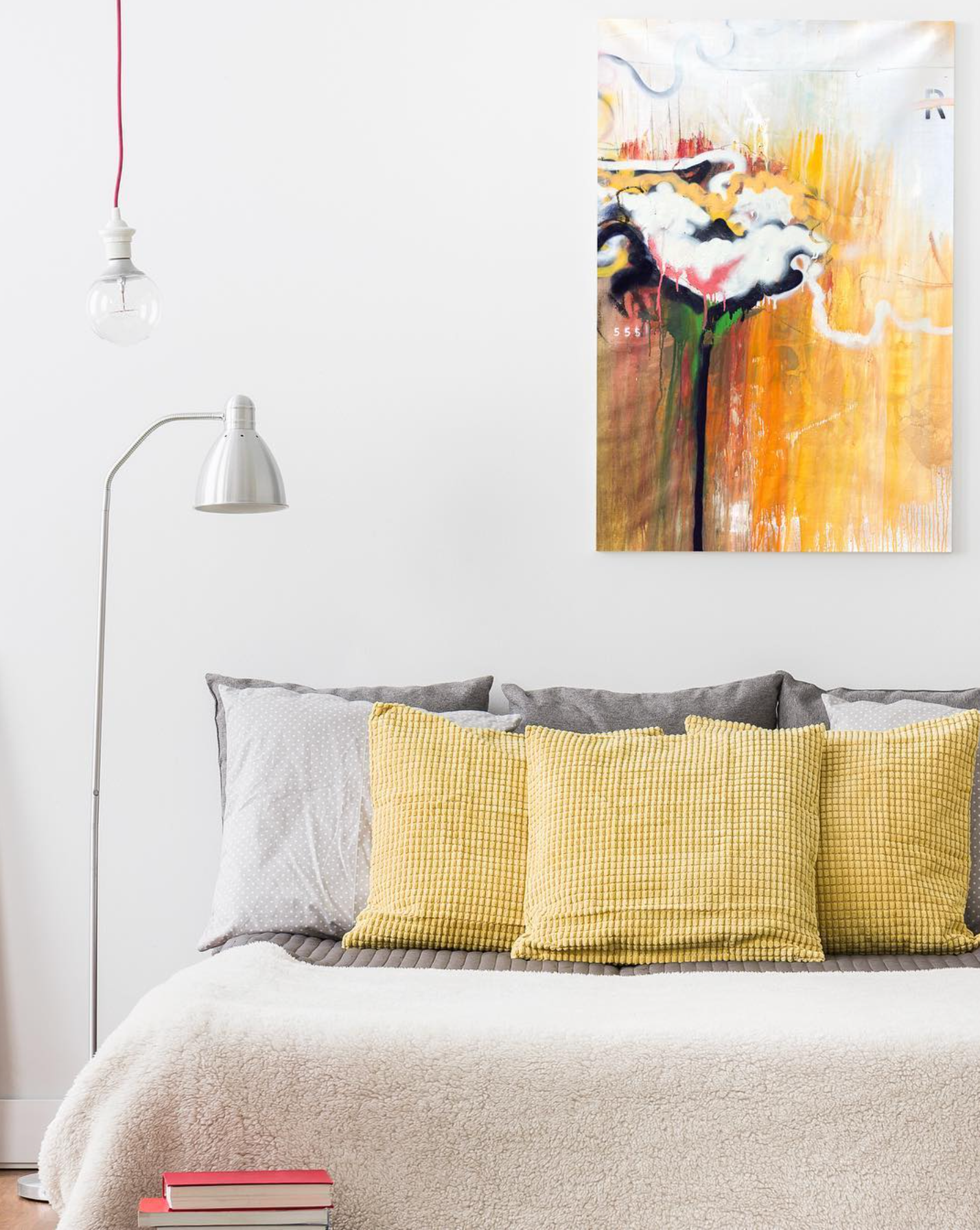 Cozy bed with yellow accent pillows against a white wall, paired with a warm-toned abstract floral artwork in orange, pink, and cream